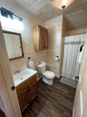 Ein Badezimmer mit Holzwandverkleidung, einem weißen Waschbecken, einer Toilette und einer Duschvorhang.