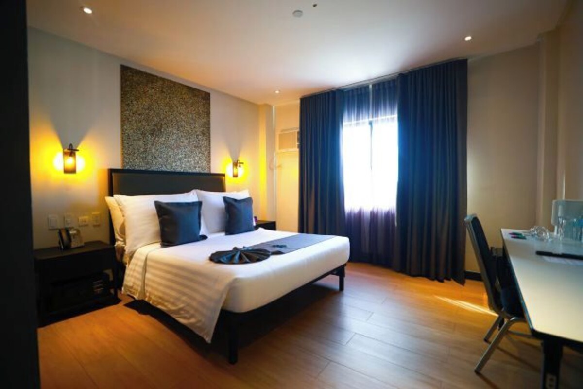 A hotel room with a large bed, two bedside lamps, a desk with a chair, and a window with curtains.