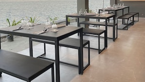 Un espace de restauration en plein air, avec des tables et des chaises, offrant une vue sur un plan d’eau et sur des collines lointaines.