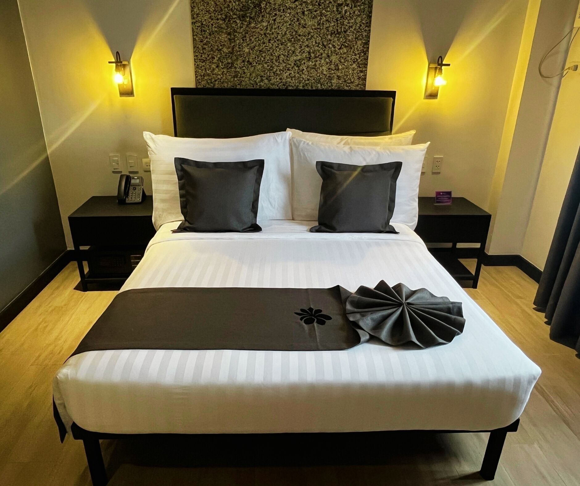 A neatly made bed with white linens and two dark pillows, a black headboard, and two bedside tables with lamps.