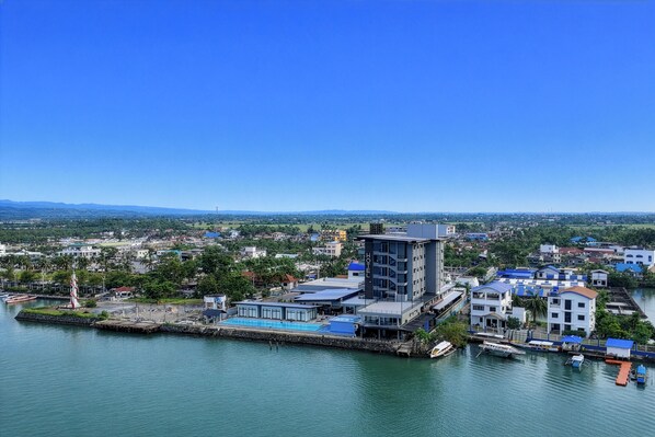 Un hotel costero de diseño moderno, con una torre destacada, piscina y un puerto deportivo con barcos.