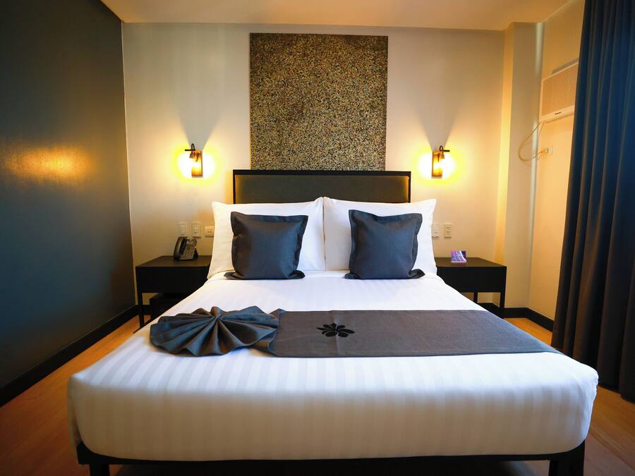 A hotel room with a large bed, two bedside tables, a wall-mounted artwork, and a curtain.
