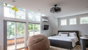 Camera da letto con un letto grande, una poltrona sacco rotonda, una televisione e un balcone con vista sul verde.