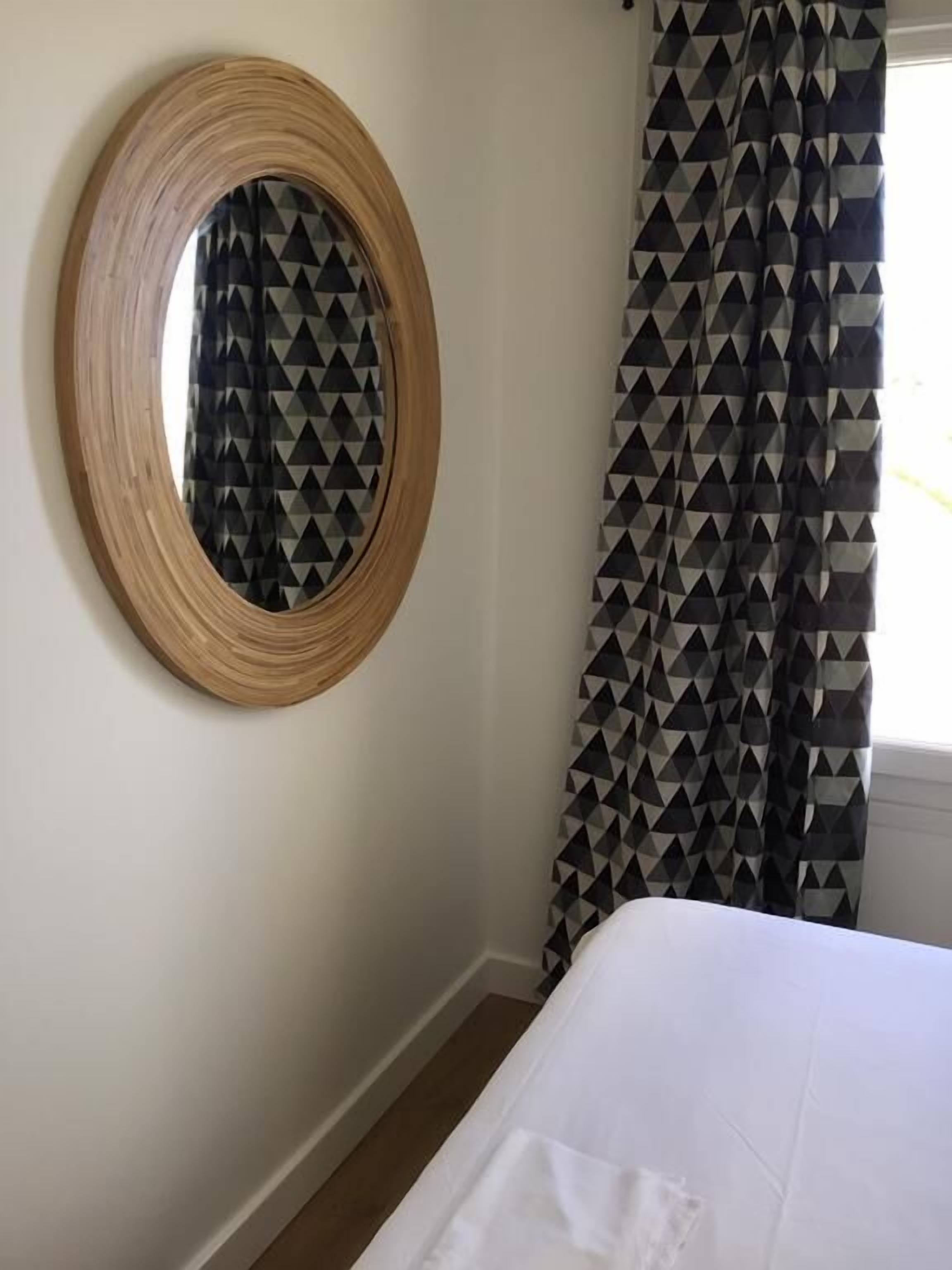 A bedroom with a bed, a round mirror, and patterned curtains.
