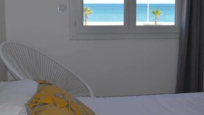 Un dormitorio con una cama, una silla blanca y una ventana con vistas al mar.