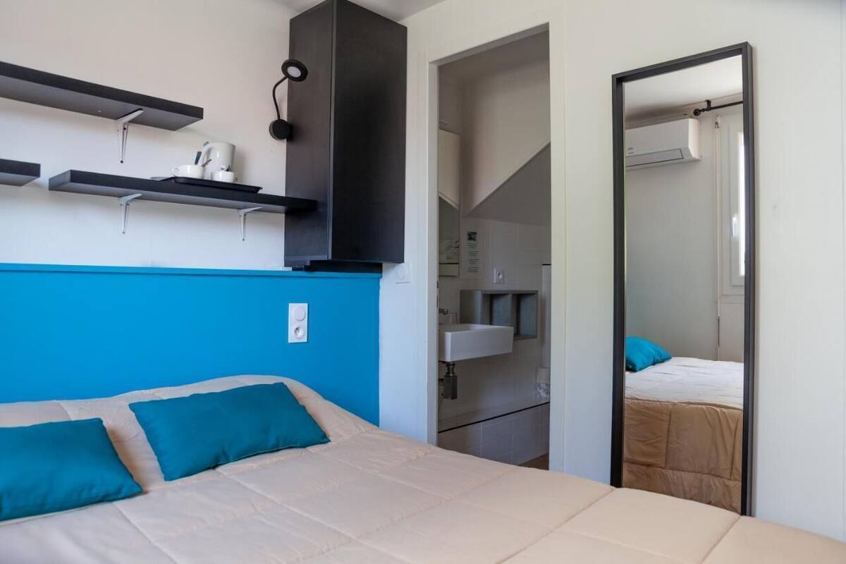 Hotellihuone, jossa on sänky, peili, pieni keittiö ja kylpyhuone.