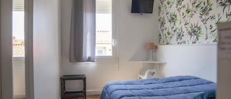 A bedroom with a bed, a TV, a radiator, and a window with curtains.