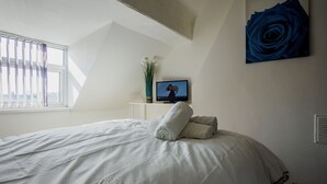 A bedroom with a large bed, a television on a stand, a vase with flowers, and a blue rose painting on the wall. - WoodHus Lodge Lovely Specious Room 5 (Stoke-on-Trent)