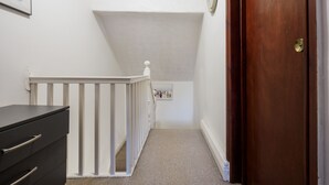 A narrow hallway with a wooden door on the right, a white railing, and a small shelf with figurines. - WoodHus Lodge Lovely Specious Room 5 (Stoke-on-Trent)