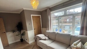 Un salon avec un canapé, une plante en pot, une porte en bois et une fenêtre avec des rideaux.