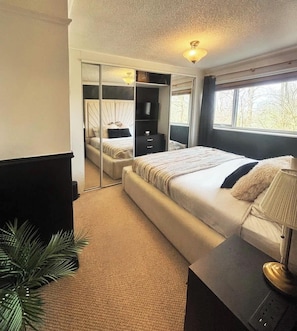 A bedroom with a bed, bedside table, lamp, and a mirror.