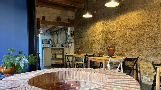 Ein rustikales Interieur mit einem runden Kamin aus Ziegelsteinen, Holztischen und -stühlen.