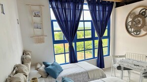 Ein Schlafzimmer mit zwei Betten, einem großen Fenster mit blauen Vorhängen, einer Wanduhr und einem weißen Heizkörper.