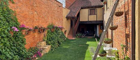 A narrow courtyard with a brick wall, a small garden, and a building with a tiled roof.