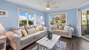 Ein Wohnzimmer mit zwei beigefarbenen Sofas, einem weißen Couchtisch und einem Deckenventilator.