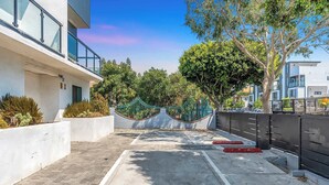 A modern building with a paved walkway, a green bridge, and a tree-lined area. - Luxury Townhome w/ Gated Parking & Private Balcony (Los Angeles)