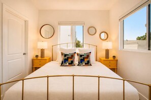 A hotel room with a bed, two bedside tables, a window, and a door.