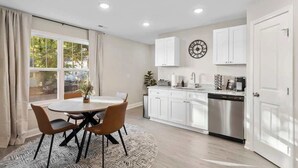 Une cuisine moderne avec des meubles blancs, un lave-vaisselle en acier inoxydable et un coin repas comprenant une table ronde et des chaises.