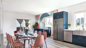 Een moderne keuken met een inbouwkoelkast, een eethoek met roze stoelen en een blauwe bank.