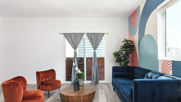 Een moderne woonkamer met een blauwe bank, twee oranje fauteuils en een houten salontafel.