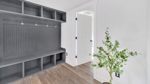 Un couloir avec un banc intégré de couleur grise, une porte blanche et une plante en pot.