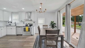 Une cuisine moderne avec des meubles blancs, des appareils en acier inoxydable et un coin repas comprenant une table et des chaises en bois.