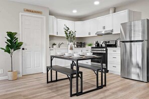 Uma cozinha moderna com armários brancos, uma geladeira de aço inoxidável e uma mesa de jantar posta para quatro pessoas.