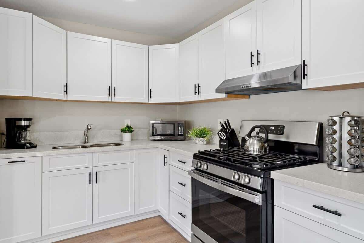 Una cocina moderna con armarios blancos, estufa a gas, microondas y cafetera.