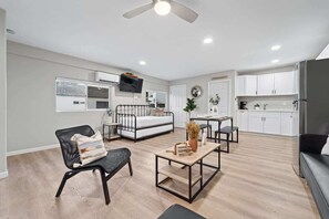 Um apartamento moderno com cozinha compacta, área de jantar, sala de estar com sofá e poltrona, e ventilador de teto.