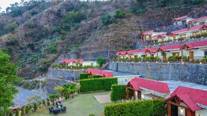 Un hôtel situé sur une colline, composé de plusieurs bâtiments aux toits rouges, doté de murs en pierre et d’un jardin bien entretenu avec des espaces aménagés pour se détendre.