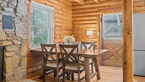 A wooden interior with a stone wall, a dining table with chairs, and a window with blinds.