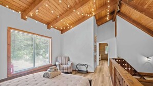 A bedroom with a large bed, wooden ceiling beams, a chair, and a staircase.