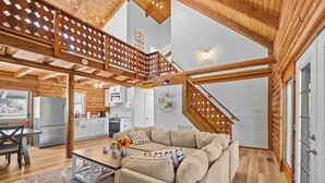 A spacious living area with a wooden ceiling, a sofa, a dining table, and a kitchen in the background.