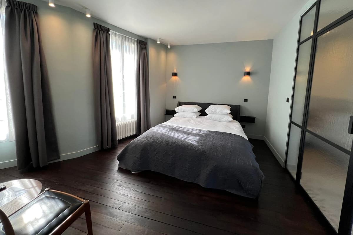 A modern hotel room with a large bed, a wooden floor, and a view of the city through a large window.