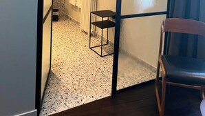 A modern bathroom with a white tiled floor, a black metal shelf, and a towel rack. - Le Petit Château (Baye)