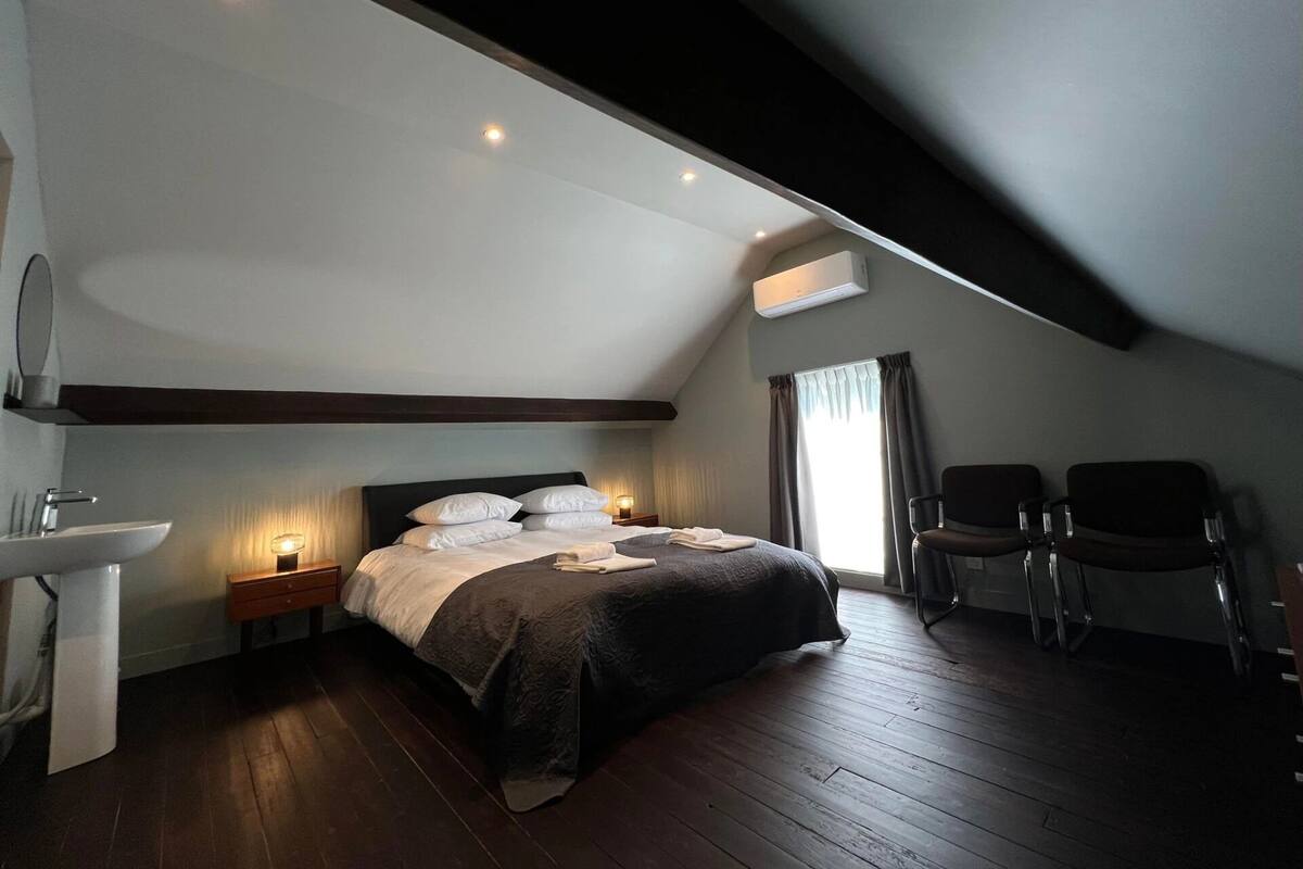 A bedroom with a bed, bedside tables, a sink, and two chairs.