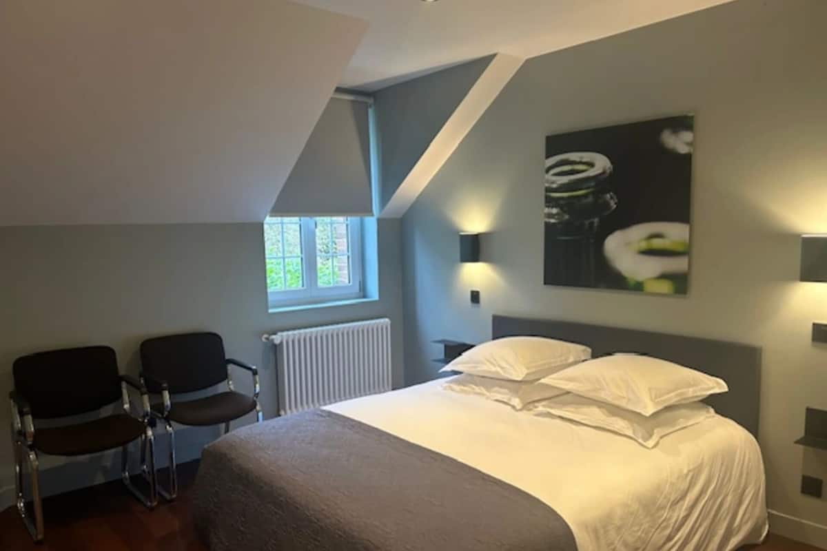 A bedroom with a bed, two chairs, a window, and a radiator.
