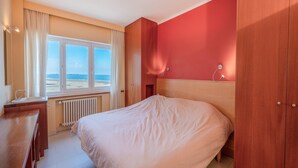 Ein Schlafzimmer mit einem großen Bett, einem Fenster mit Blick auf den Strand, einem Holzschrank und einem Schreibtisch mit Spiegel.