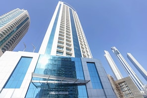 Un immeuble de grande hauteur doté d’une façade moderne en verre et d’une entrée imposante surmontée d’un auvent en métal.