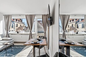 Ett modernt hotellrum med en matplats, stora fönster med gardiner, en platt-TV och utsikt över stadssiluetten.