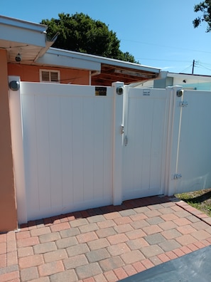A white metal gate with a security camera and a sign indicating it is a security gate.