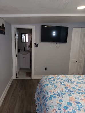 A bedroom with a bed, a television mounted on the wall, a door, and a bathroom visible through an open doorway.
