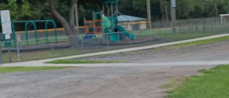 A gravel path leading to a playground with a slide and climbing structures.