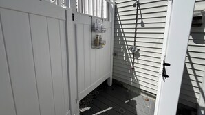 A white wooden fence with a metal gate, a small outdoor shelf with toiletries, and a metal hose attached to the wall. - Family friendly and dog welcoming home, minutes from the beach in Old Orchard! (Old Orchard Beach)