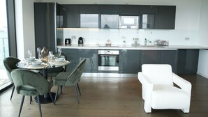 Une cuisine moderne avec des meubles de couleur sombre, un four encastré et un coin repas comprenant une chaise blanche et une table dressée pour deux personnes.