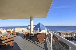 A covered outdoor area with wicker furniture and a blue umbrella, overlooking the ocean. - Meridian 901 West by Seaside Vacations & Sales (Ocean City)