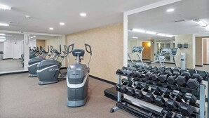 Un gimnasio con cintas de correr, elípticas y un estante con mancuernas.
