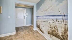 Un pasillo con un mural de playa, una puerta blanca y baldosas color beige.