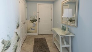 Un couloir avec une porte blanche, un miroir, une lampe et une petite table ornée d’objets décoratifs.