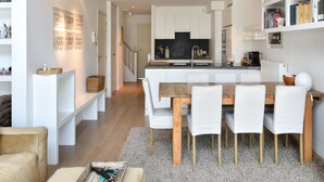 A modern kitchen with white cabinets, a central island, and a dining area with a wooden table and white chairs. - Duplex at Albert Beach With Stunning Sea Views (Knokke-Heist)